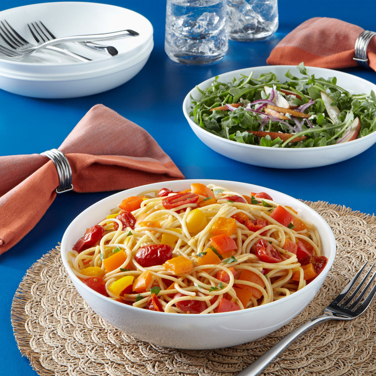 pasta with tomatoes on table with salad in a second bowl